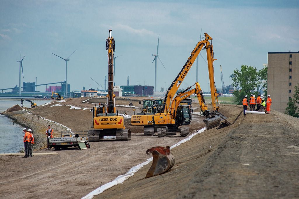 Three excavators pile up dirt to raise the level of a sea dike near Defzijl, Netherlands.