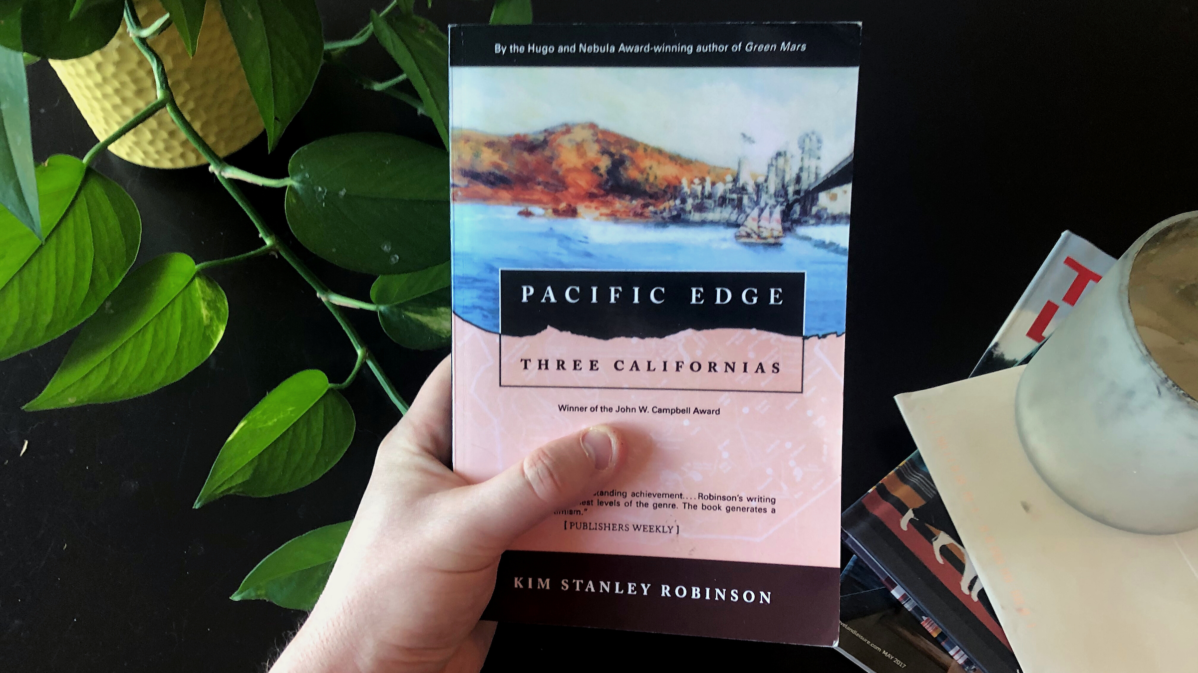 A photo of someone holding Pacific Edge by Kim Stanley Robinson over a coffee table.