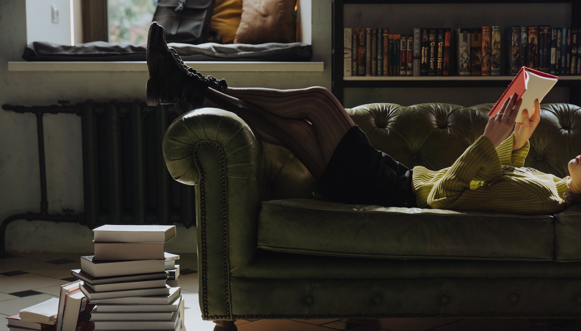 A woman reclines on a sofa reading a book.